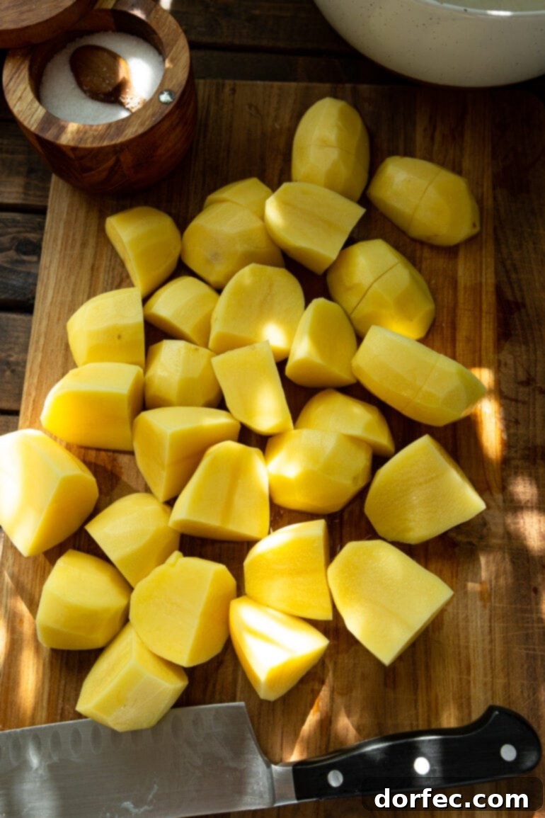 Several peeled and uniformly quartered Yukon Gold potatoes neatly arranged on a rustic wooden cutting board, ready for the Instant Pot. This image highlights the fresh, quality ingredients for the perfect mashed potatoes.