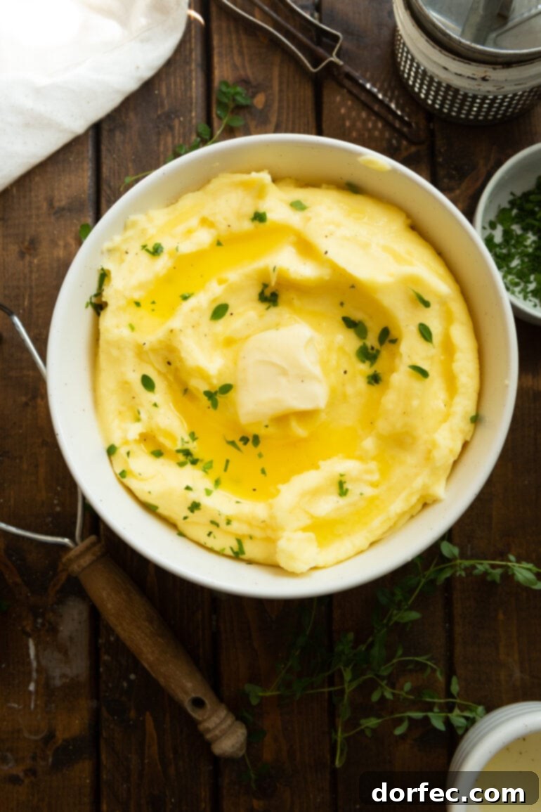 A large, rustic serving bowl brimming with creamy, golden mashed potatoes, generously topped with a melting pat of butter and a scattering of fresh green herbs, signaling deliciousness and comfort.