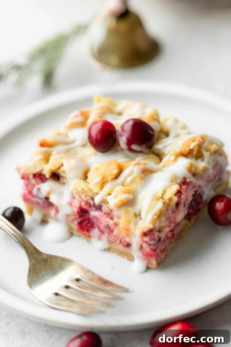 A photo of a cranberry bar sitting on a white dessert plate topped with a golden crumble and a white glaze