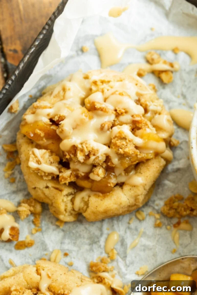 A golden-baked Apple Crisp Cookie, generously topped with cinnamon apple pie filling, a crunchy buttery oat crumble, and a delicate vanilla glaze drizzle.
