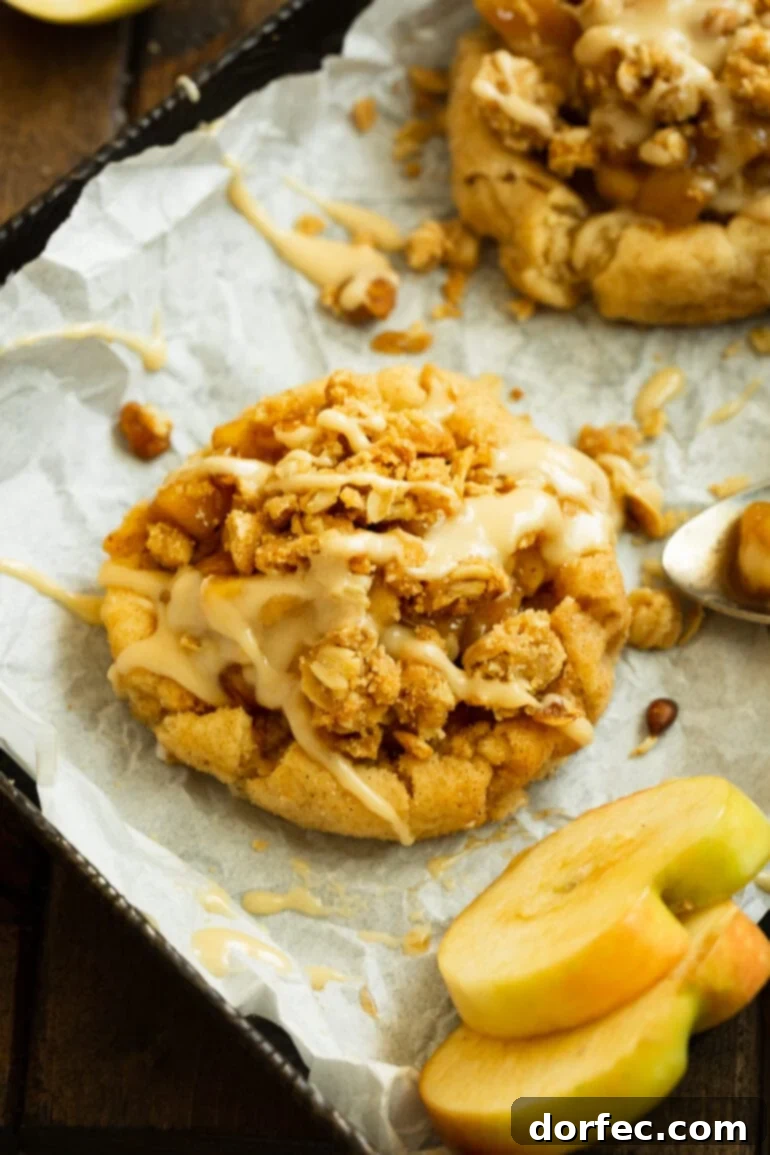 A close-up photo of an Apple Crisp Cookie, showcasing its luscious cinnamon apple filling, golden-brown crunchy oat topping, and delicate vanilla glaze.