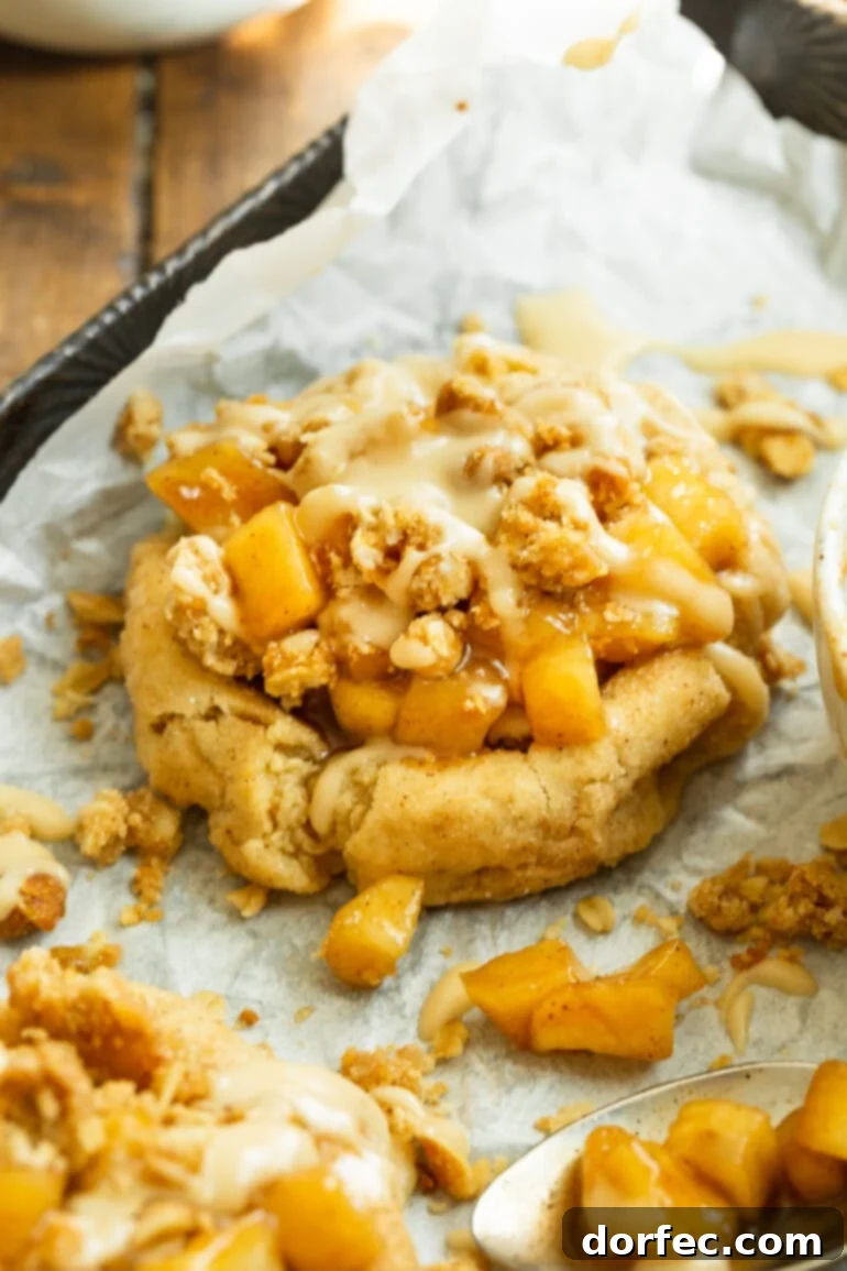 A beautifully plated Apple Crisp Cookie, showcasing its golden cookie base, warm apple filling, crunchy oat topping, and a delicate drizzle of vanilla glaze.
