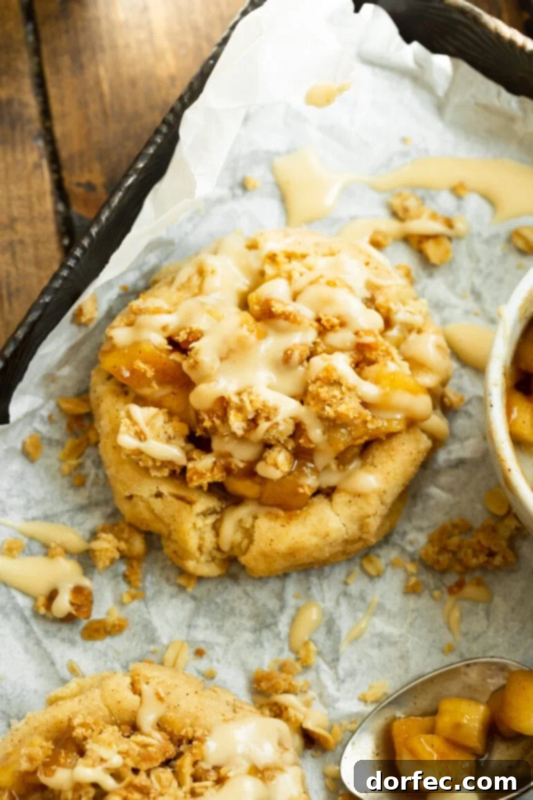 A vibrant, mouth-watering image of an Apple Crisp Cookie, featuring a perfectly golden-brown cookie base, a mound of spiced apple filling, a crunchy oat crumble, and a tantalizing vanilla glaze.