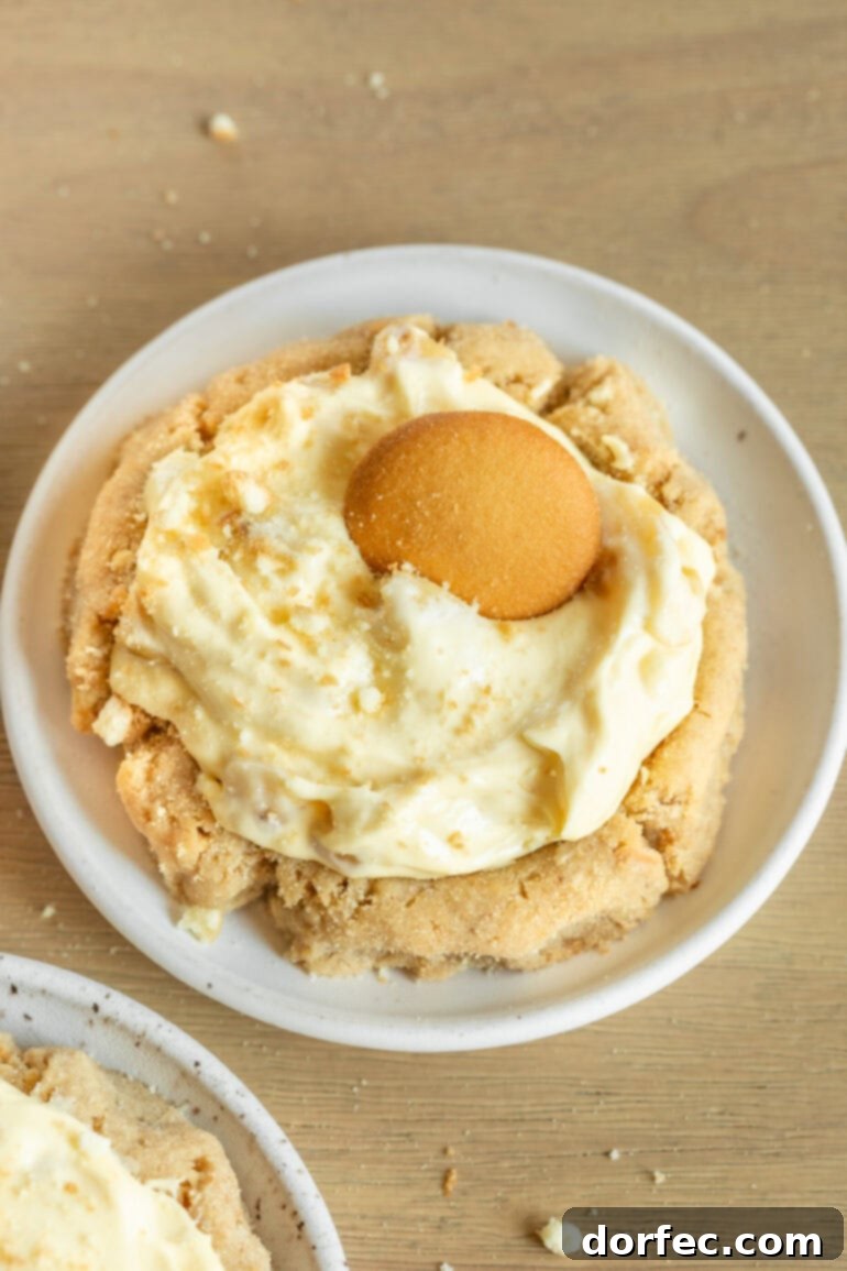Giant Banana Cream Pie Cookies 4 a photo of a banana cream pie cookie with a cookie base topped with creamy banana pudding topped with a nilla wafer sitting on a small white dessert plate