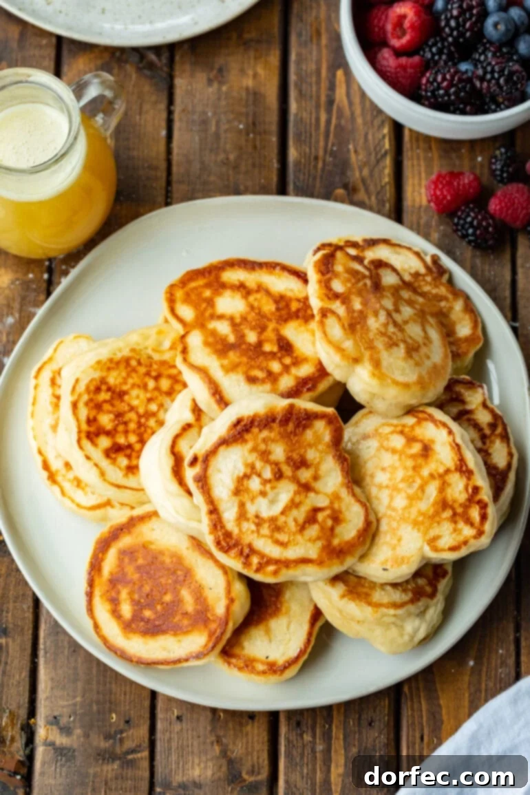 A photo of a large white plate generously piled with golden, crispy Oladi pancakes, with a small pitcher of creamy buttermilk syrup elegantly placed beside it.