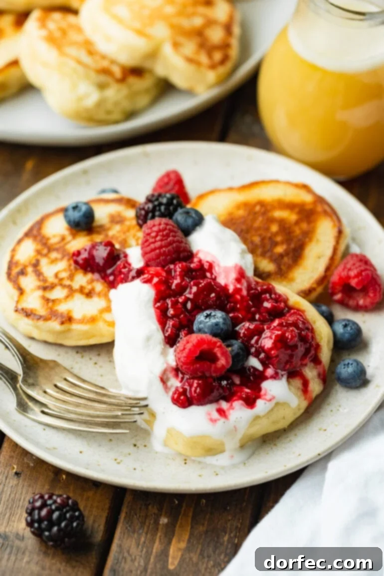 A vibrant photo of three crispy golden Oladi pancakes on a plate, lavishly topped with an assortment of mixed fresh berries and a cloud of fluffy whipped cream.