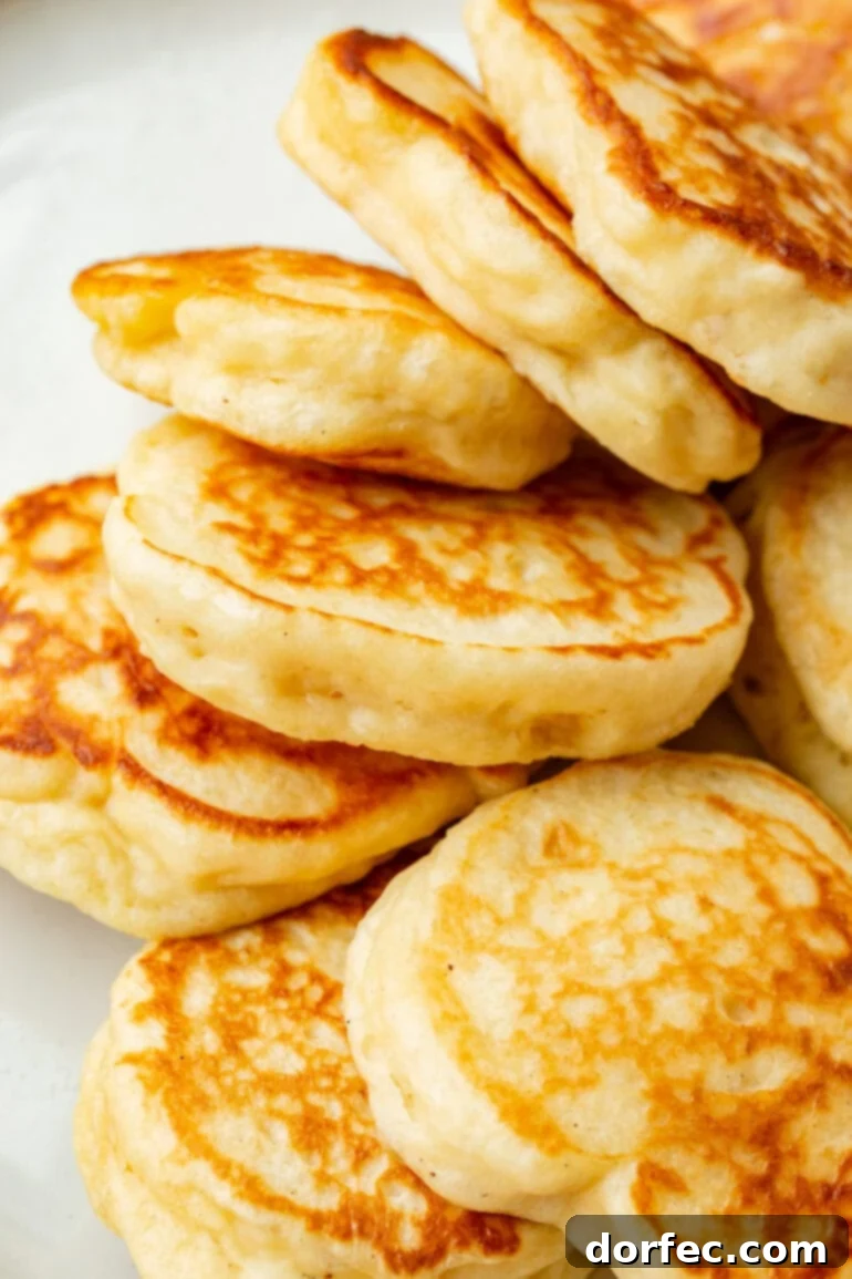 A stack of perfectly golden, fluffy Oladi pancakes piled high on a white plate, ready to be served and enjoyed.