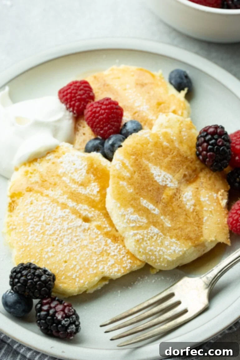 Fluffy Japanese Soufflé Pancakes 3 A stunning plate overflowing with golden-brown, fluffy Japanese cloud pancakes, artfully adorned with a generous dusting of powdered sugar, a drizzle of maple syrup, and a vibrant scattering of fresh mixed berries.