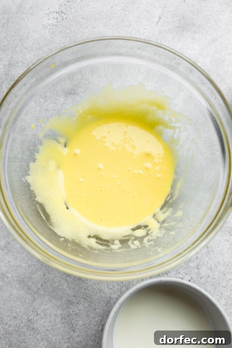 Fluffy Japanese Soufflé Pancakes 5 A close-up shot of a creamy, pale yellow egg yolk mixture resting in a large glass bowl, patiently awaiting the addition of other ingredients. Its smooth consistency indicates proper whisking and preparation.