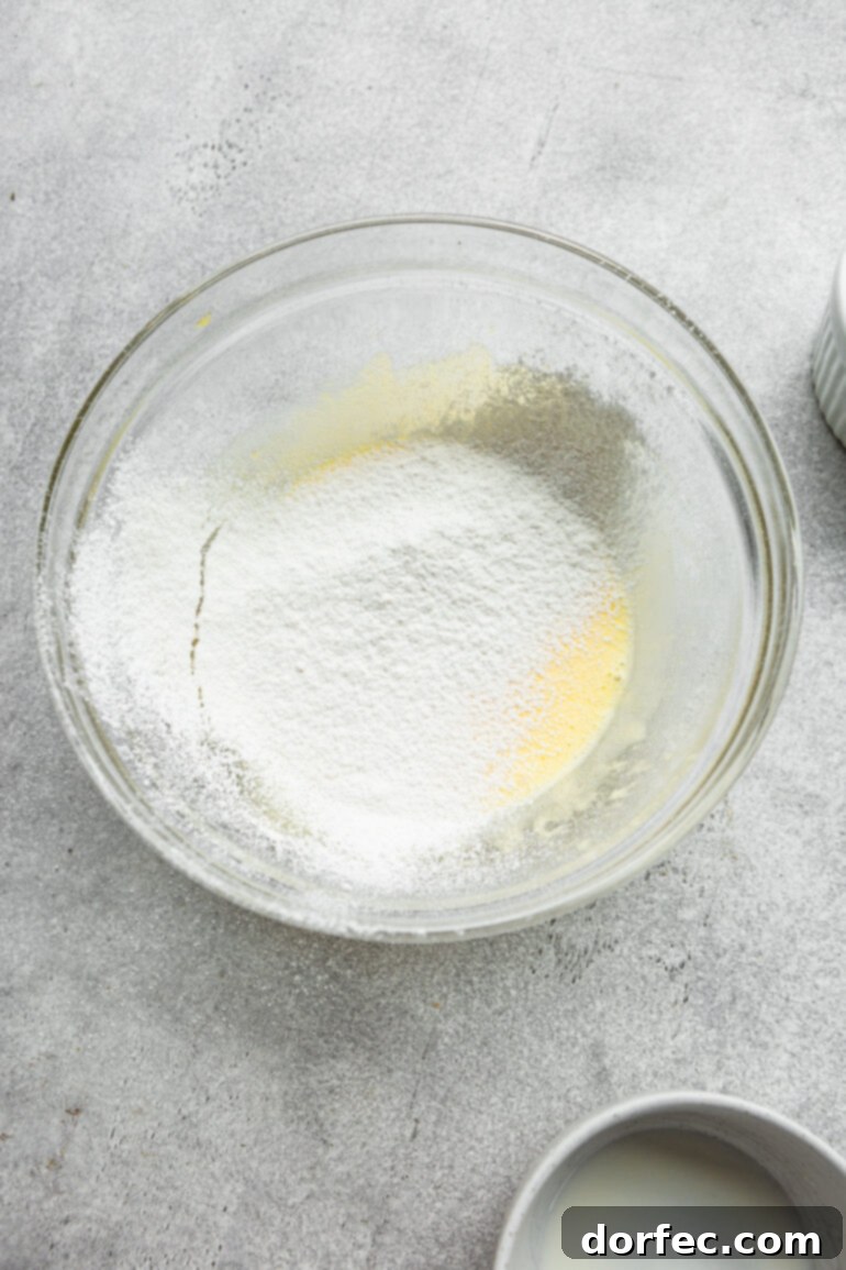 Fluffy Japanese Soufflé Pancakes 6 A visual step-by-step: fluffy Japanese cloud pancake batter in a large glass bowl, with finely sifted flour and other dry ingredients artfully added, showing the initial stages of combination before the delicate folding process begins. This image captures the texture and readiness of the batter for the next step.