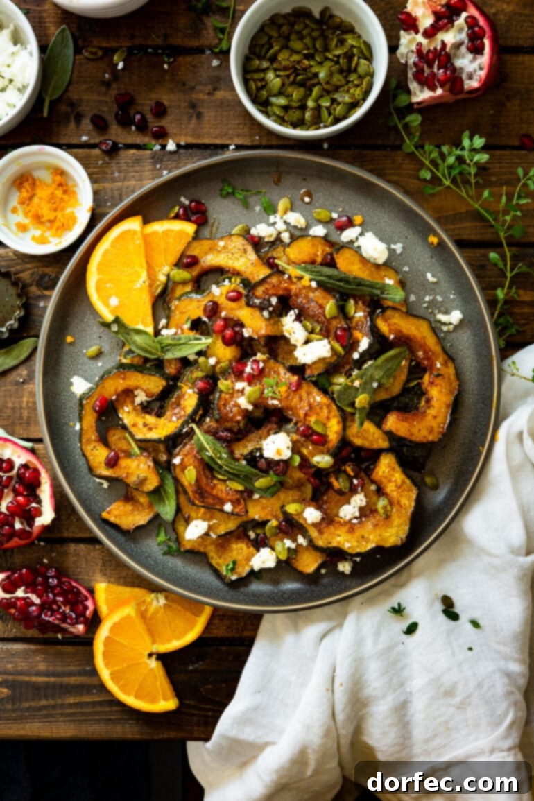 Heartwarming Holiday Acorn Squash 11 A large, beautifully arranged serving plate overflowing with holiday acorn squash, generously topped with creamy feta, crispy fried sage leaves, and vibrant pomegranate seeds, with fresh orange slices on the side.