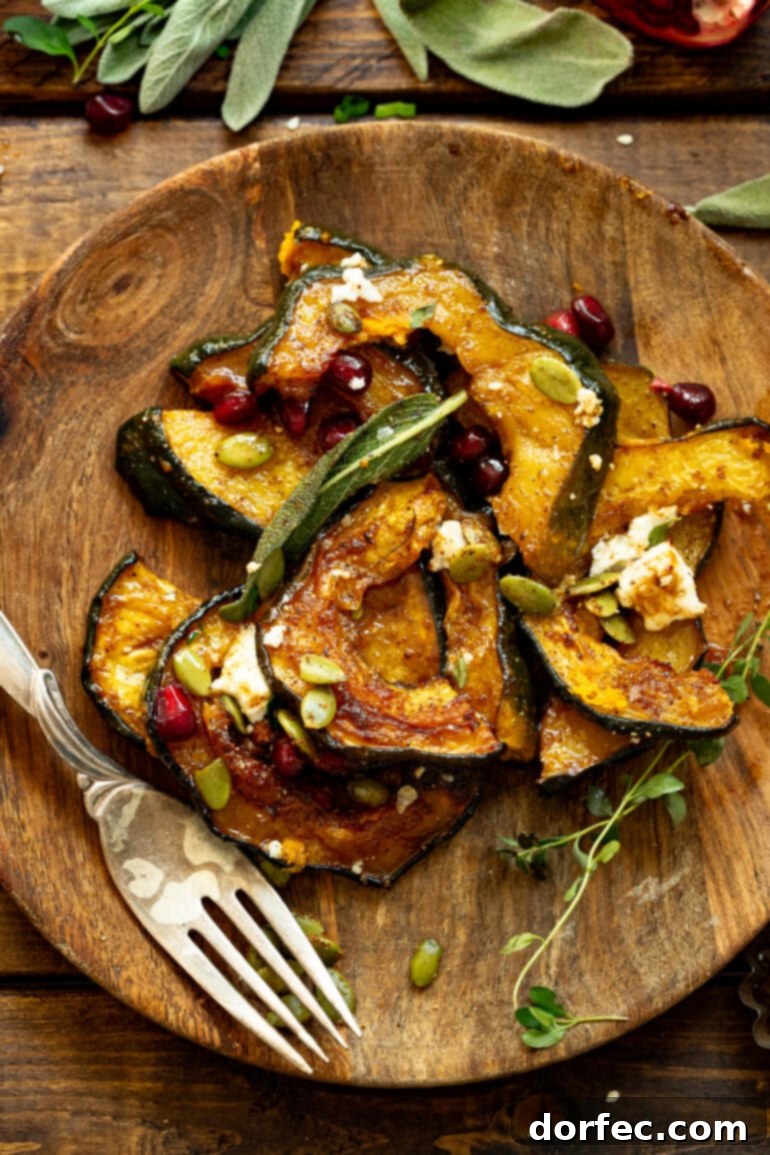 Heartwarming Holiday Acorn Squash 3 A photo of several slices of roasted acorn squash on a rustic wooden plate, garnished with crumbled feta, bright pomegranate seeds, crunchy pepitas, and crispy fried sage leaves.