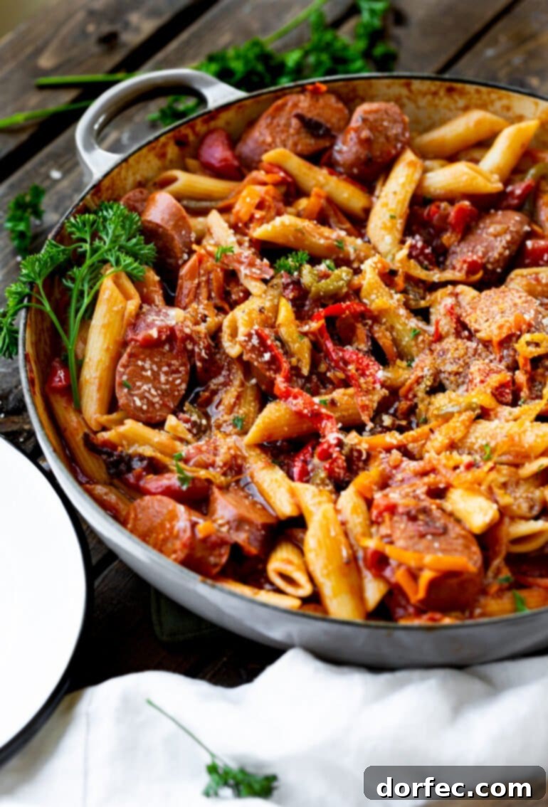 A close-up photo of a cast iron skillet brimming with freshly cooked skillet Italian sausage, colorful bell peppers, and onions, all perfectly mixed with penne pasta and a savory sauce, ready to serve for a weeknight dinner.