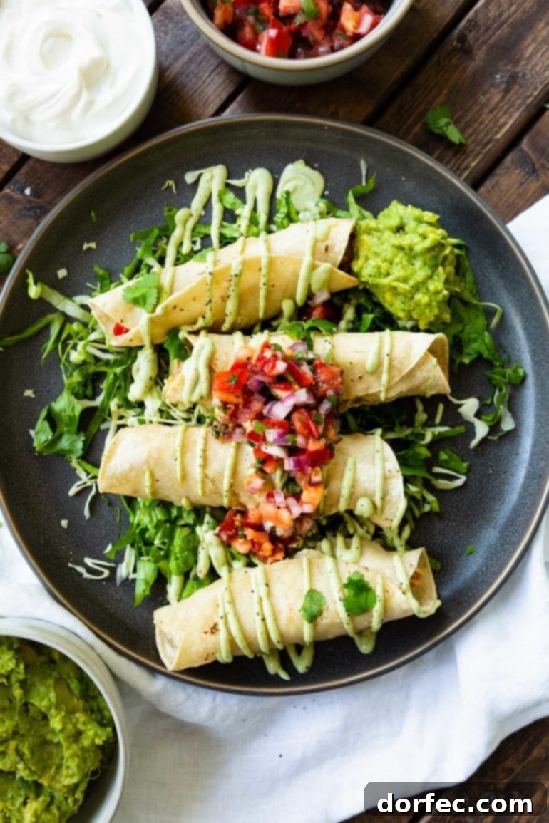 A beautifully arranged dark plate showcasing crispy baked chicken taquitos, elegantly drizzled with creamy avocado crema over a bed of fresh lettuce and topped with vibrant pico de gallo, ready for an easy Mexican dinner.