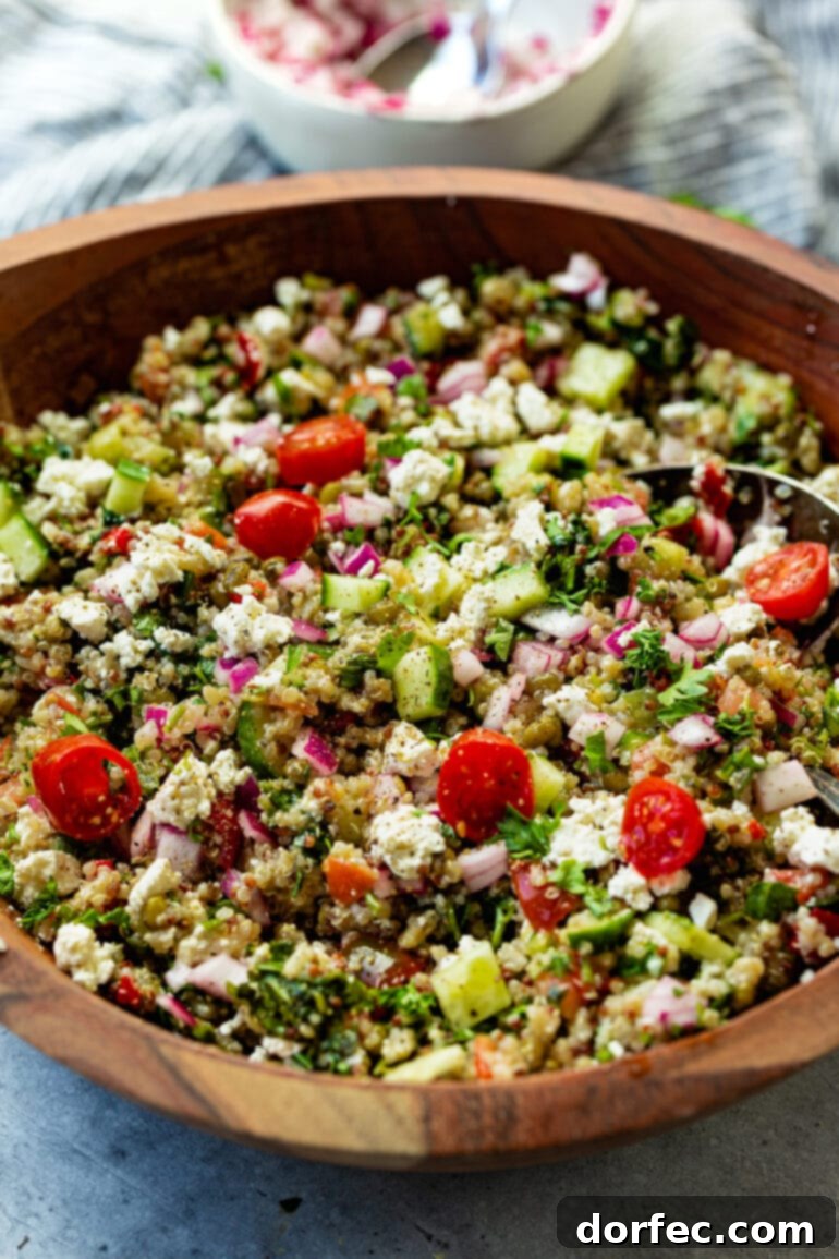 A beautifully presented Mediterranean Quinoa Salad in a large wooden serving bowl, filled with colorful ingredients including fluffy quinoa, ripe tomatoes, crisp cucumber, red onions, and an assortment of fresh herbs like parsley and mint.