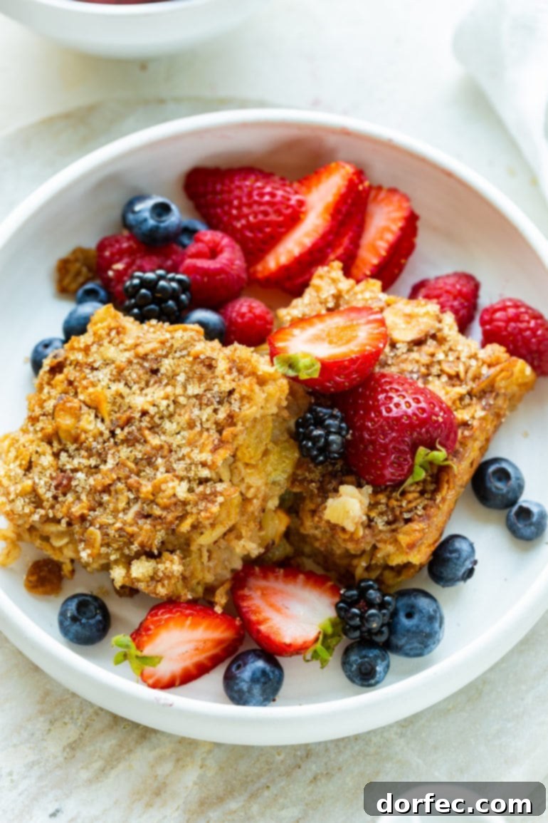 Two generous slices of gourmet Creme Brulee Baked Oatmeal, nestled in a white bowl and beautifully surrounded by an assortment of fresh mixed berries, perfect for a luxurious weekend breakfast or brunch.