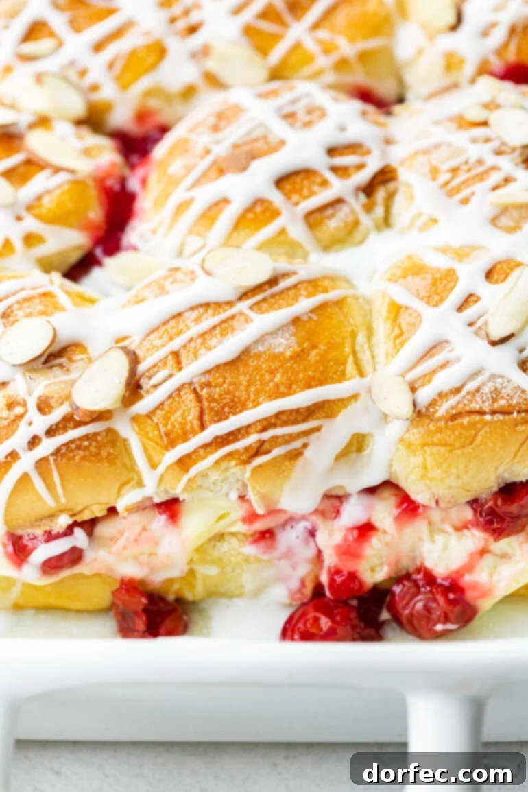 A baking dish filled with an array of golden-brown cherry cheese danish sliders, featuring a rich cherry pie filling and creamy cheesecake filling, generously topped with a sweet drizzle and toasted sliced almonds.