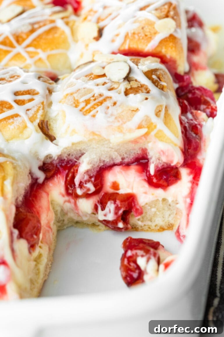 A baking dish displays a selection of baked cherry cheesecake sliders, with one slider carefully removed to reveal the layers of sweet cherry pie filling and creamy cheesecake filling spilling out, showcasing the delightful interior.