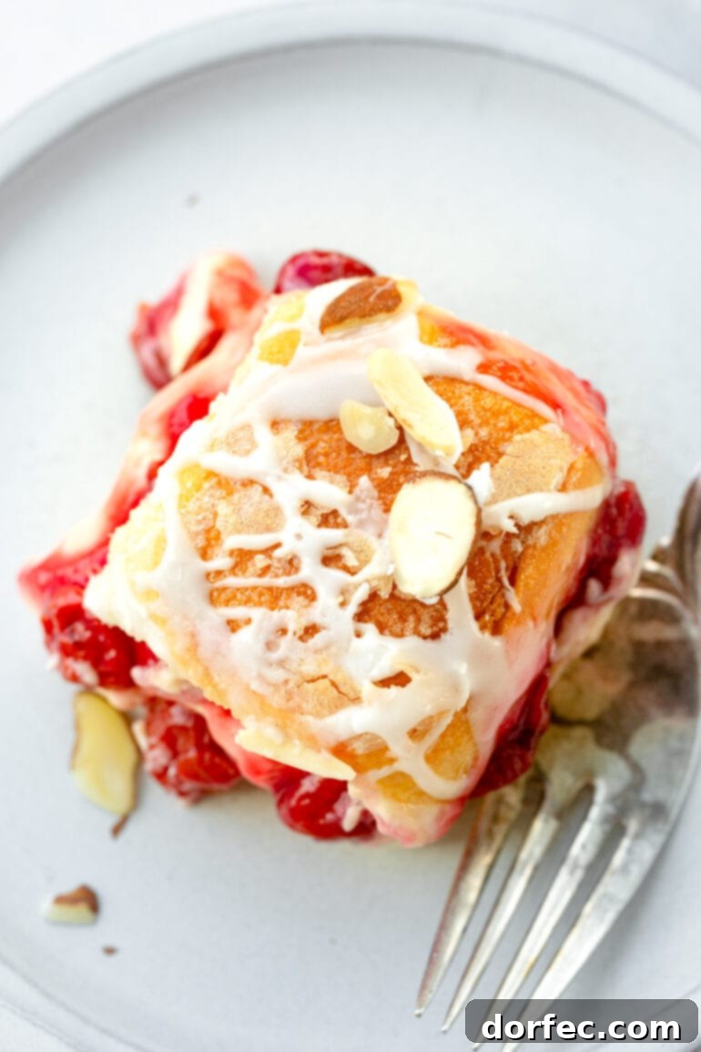 An overhead view of a single golden-baked cherry cheese danish slider, adorned with a delicate creamy white glaze and garnished with toasted sliced almonds, ready to be enjoyed.