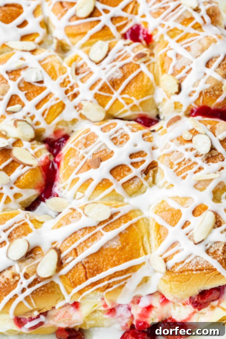 A baking dish showcases a dozen golden-baked cherry cheese danish sliders, each beautifully topped with a creamy white drizzle and a sprinkle of sliced almonds, creating an appetizing display.