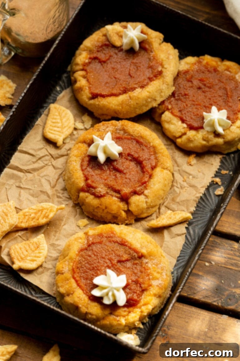Delightfully Soft Chewy Pumpkin Pie Spice Cookies 3 A close-up shot of several unbaked pumpkin pie cookies with small wells pressed into their centers, sitting on a baking sheet lined with crumpled brown parchment paper, ready to be filled and baked.