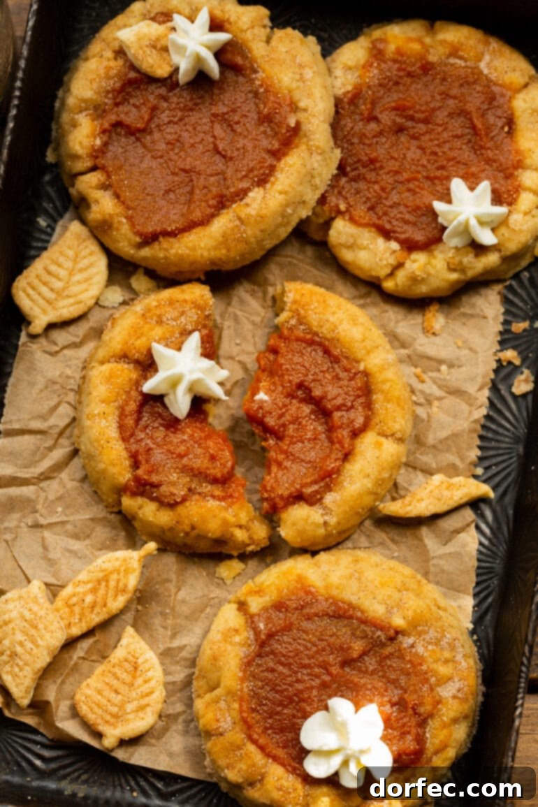 Delightfully Soft Chewy Pumpkin Pie Spice Cookies 9 A close-up shot of several pumpkin pie cookies, with one cookie expertly broken in half to reveal its soft interior and creamy pumpkin filling, all topped with a dollop of fresh whipped cream.
