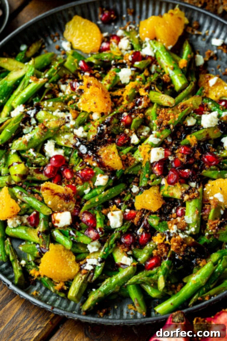 A close-up shot of the vibrant asparagus salad, beautifully plated and showcasing tender asparagus, glistening pomegranate arils, bright orange segments, crumbled Gorgonzola, and a delicate drizzle of balsamic glaze.