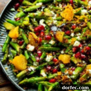 a photo of an asparagus salad mixed with oranges, pomegranate seeds and drizzled with balsamic glaze