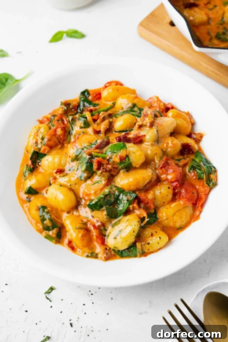 A closeup photo of a white bowl full of creamy sun dried tomato gnocchi, a comforting and flavorful pasta dish perfect for a Friday night.