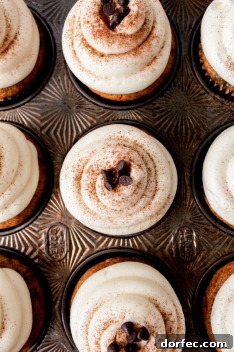 a photo taken over the top of a decorative muffin tin with baked pumpkin topped with cream cheese frosting