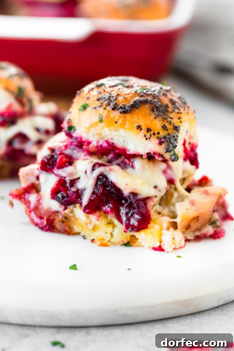 Effortless Weekly Menu November 20 to 26 7 A tempting photo of several golden-brown turkey cranberry sliders, generously coated in a glistening buttery poppyseed dressing. The image beautifully captures cranberry sauce and melted cheese delightfully oozing out from the sides of the mini sandwiches, inviting a delicious bite.