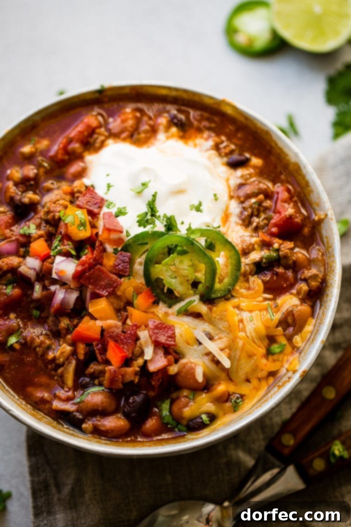 Meals for the Week: November 27 to December 3 3 Award winning healthy turkey instant pot chili. A metal bowl of ground turkey chili full of beans, chopped red onions, chopped peppers, and jalapeno slices on melted cheese, next to a dollop of sour cream with a dash of cilantro, on a grey napkin.