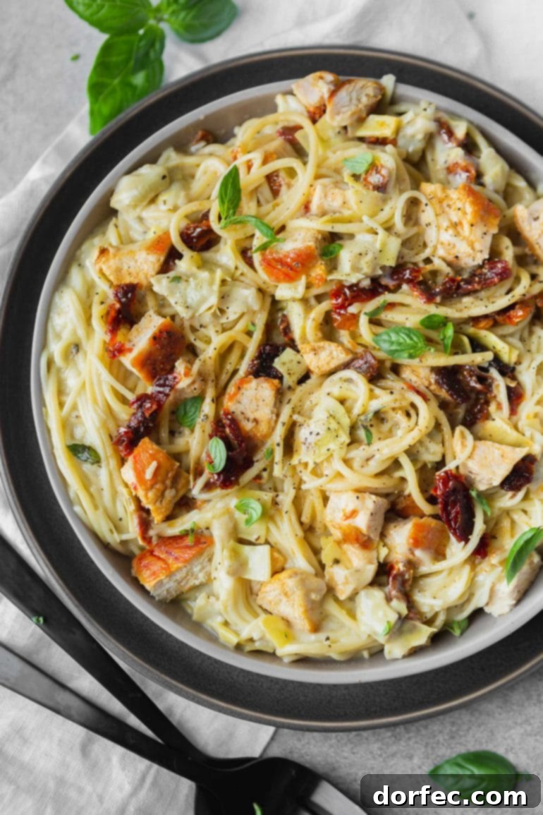 A photo of creamy chicken pasta topped with sun-dried tomatoes, golden chicken chunks, and fresh basil, highlighting a delicious and easy weeknight meal.