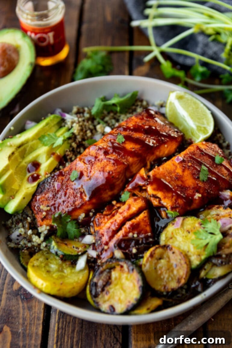 Tender Smoky Air Fryer Salmon 4 A plate featuring two succulent BBQ salmon fillets, beautifully brushed with sauce, accompanied by grilled squash and fresh sliced avocados.
