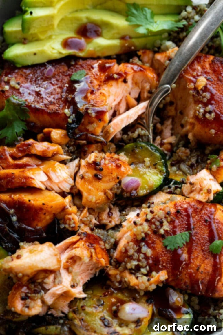 Tender Smoky Air Fryer Salmon 5 An air-fried BBQ salmon fillet, beautifully flaked apart with a fork, served over a bed of quinoa and grilled zucchini, highlighting its tender texture.