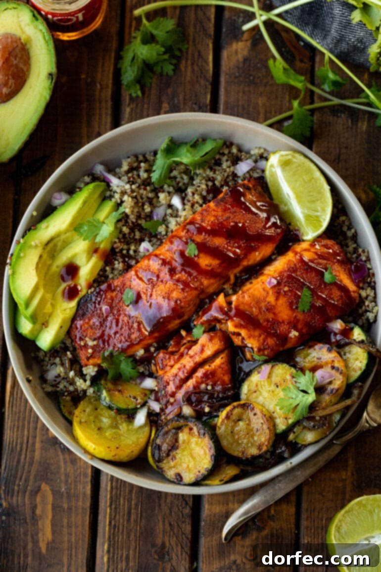 Tender Smoky Air Fryer Salmon 7 Two air-fried salmon fillets, generously brushed with BBQ sauce, presented on a plate next to grilled squash and sliced avocados, highlighting a flavorful and nutritious meal.