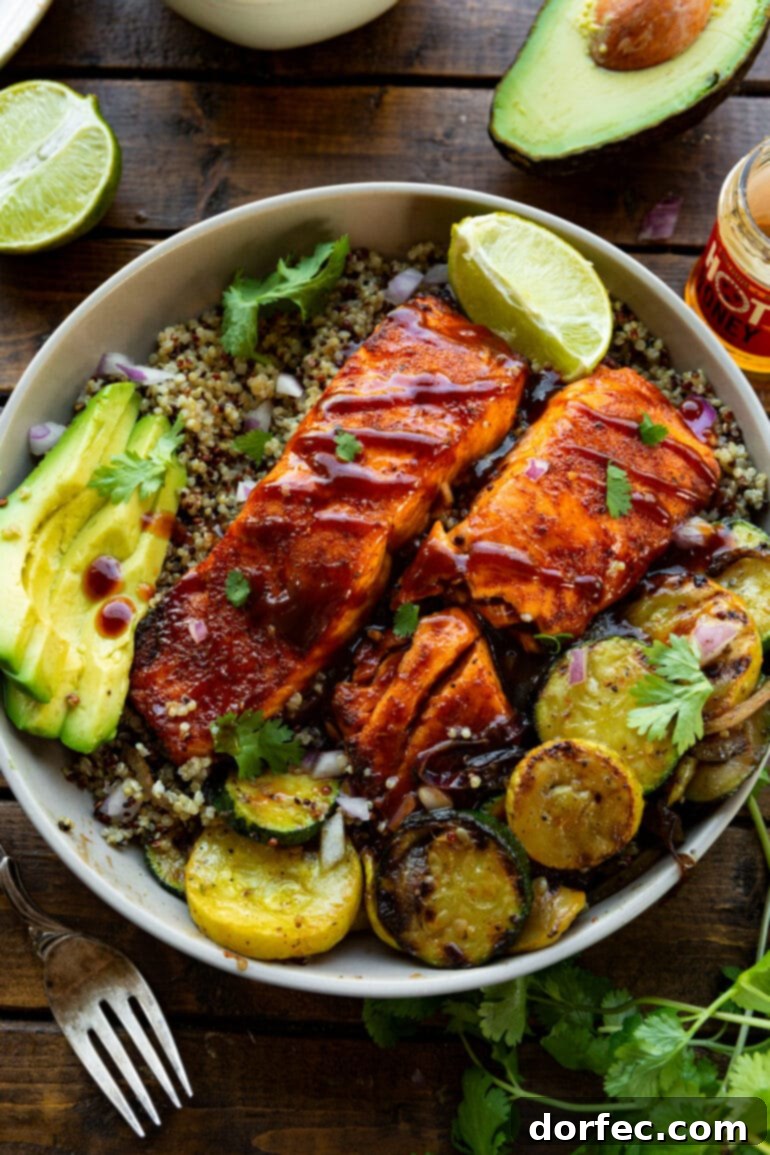 Tender Smoky Air Fryer Salmon 8 A plate of BBQ salmon resting on a bed of cooked quinoa, accompanied by grilled squash, sliced avocados, and a lime wedge, offering a complete and visually appealing meal.
