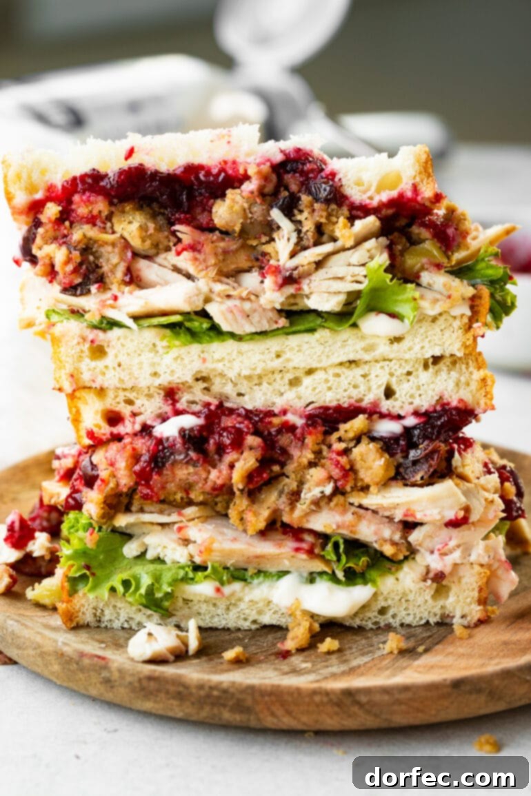 A styled photo of a Thanksgiving leftover turkey sandwich, sliced in half and stacked, revealing its rich and colorful layers.