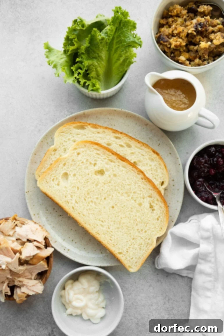 A spread of fresh ingredients for The Gobbler, including white bread, shredded lettuce, sliced turkey, a bowl of gravy, fluffy stuffing, and vibrant cranberry sauce.