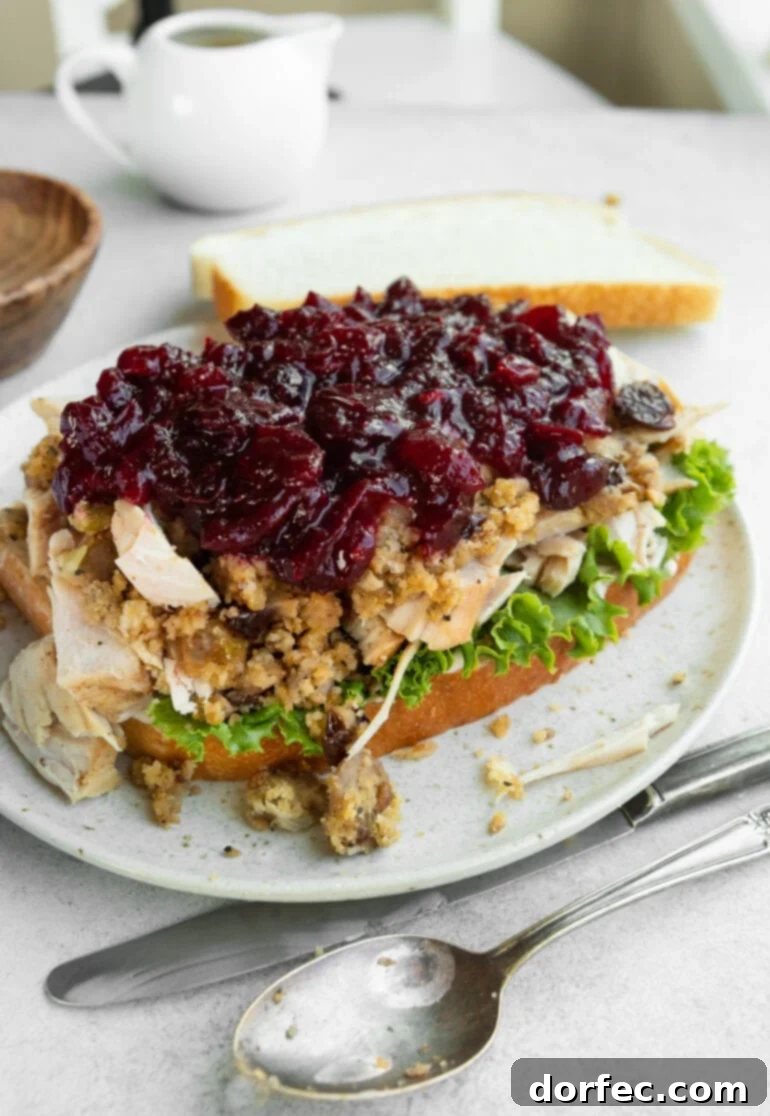 An overhead view of a deconstructed Gobbler, a Thanksgiving leftover turkey sandwich, clearly showing the distinct layers of lettuce, sliced turkey, stuffing, gravy, and cranberry sauce on a slice of white bread.