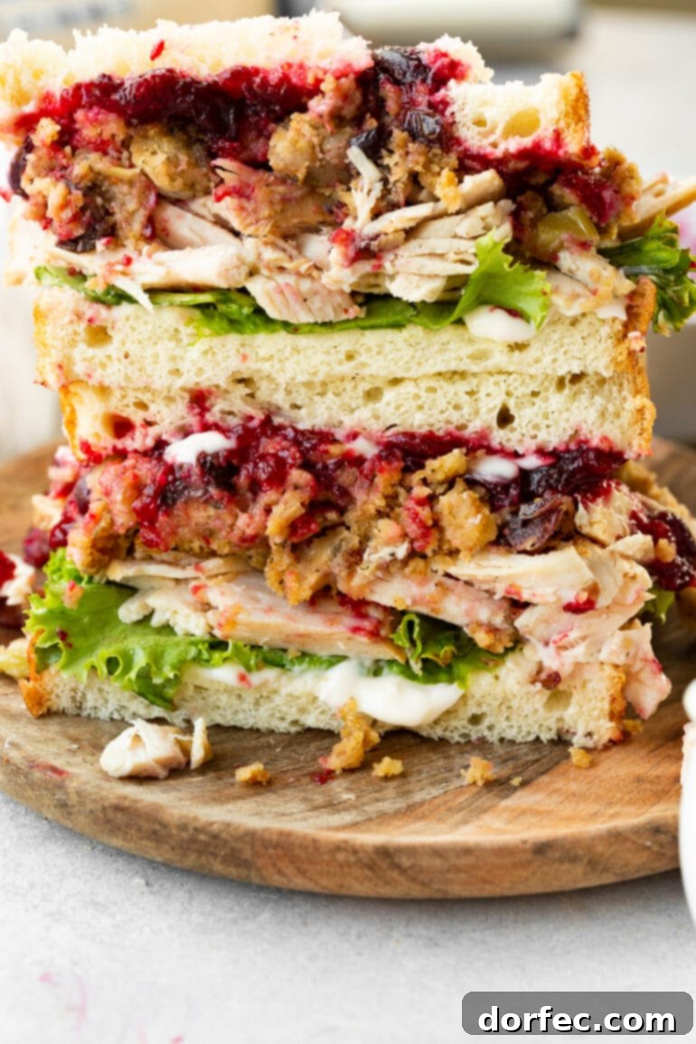 Two halves of The Gobbler, a Thanksgiving leftover turkey sandwich, stacked to showcase the abundant layers of turkey, lettuce, stuffing, cranberry sauce, and gravy.