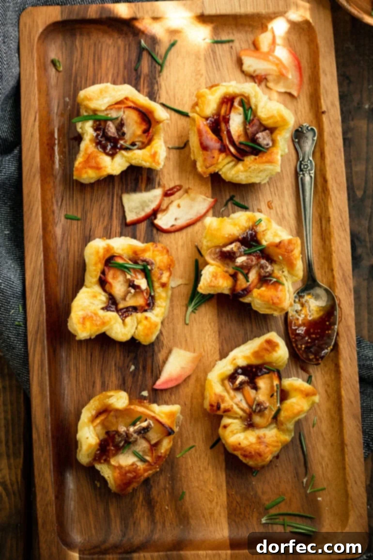 a photo taken over the top of several golden baked puff pastry bites topped with roasted apples, chopped rosemary and candied pecans