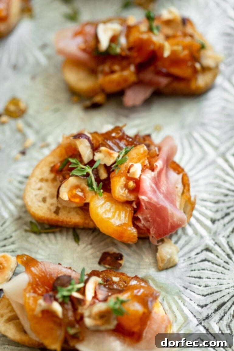 Sweet and Salty Mandarin Prosciutto Crostini 6 An appetizing overhead photo of three mandarin orange and prosciutto crostinis, each adorned with caramelized shallots, toasted hazelnuts, and fresh thyme, against a bright background.