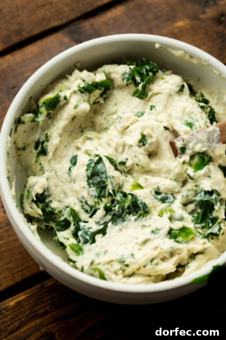A photo of a bowl brimming with creamy spinach artichoke filling, ready to be stuffed into salmon fillets.