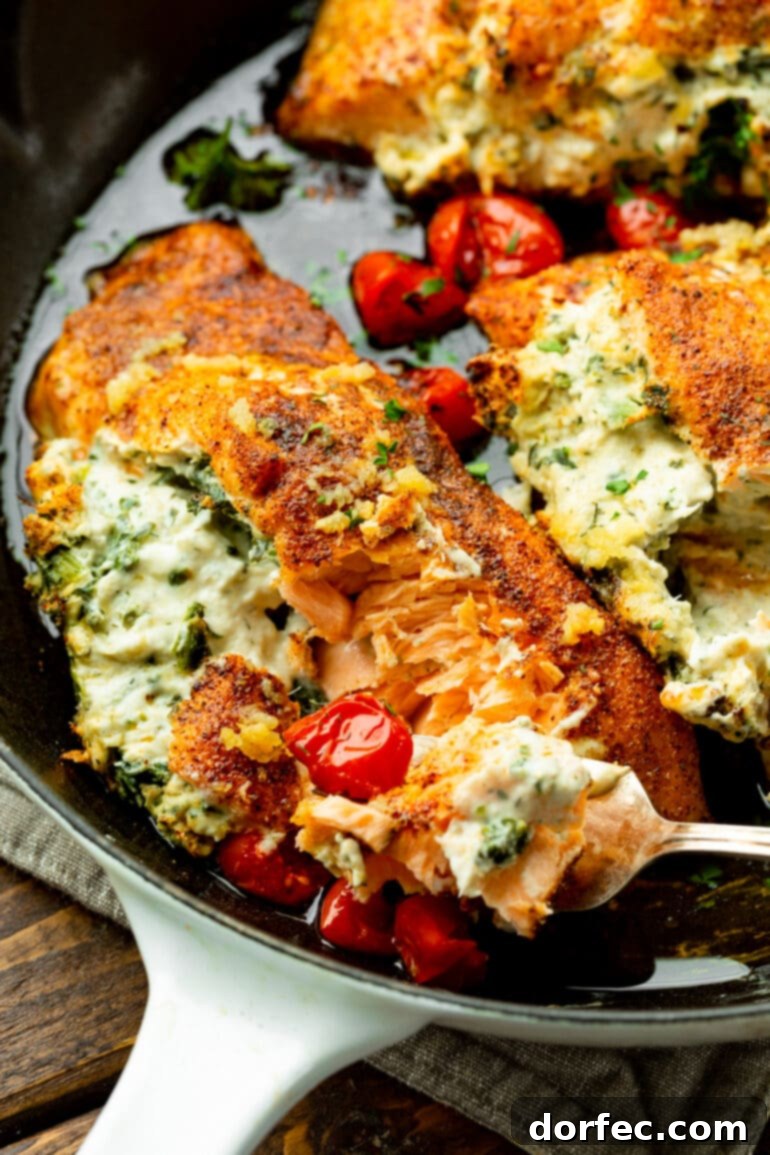 A beautifully plated creamy spinach artichoke stuffed salmon fillet, surrounded by cooked cherry tomatoes, with a fork poised to take a bite.