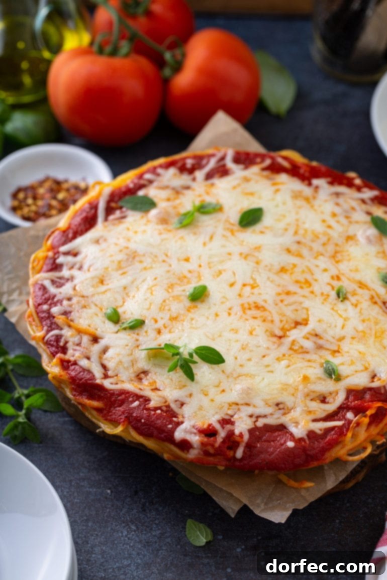 A delicious Baked Spaghetti Pie in a pie dish, featuring distinct layers of spaghetti, rich sauce, and melted cheese, garnished with fresh basil. Accompanying items include tomatoes, olive oil, red pepper flakes, and dinner plates.