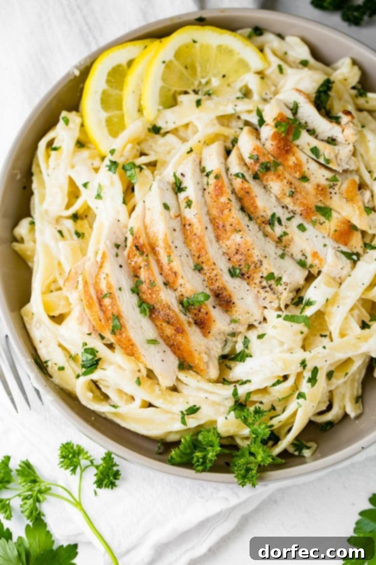 A close-up of creamy chicken fettuccine alfredo, garnished with fresh parsley, showcasing tender chicken slices atop pasta.