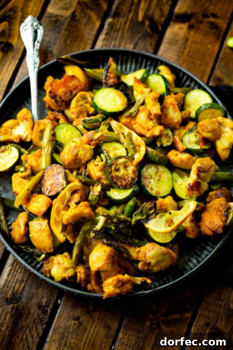 Weekly Meal Plan January 1-7 3 a photo of a dinner plate filled with bright orange-yellow bites of honey turmeric chicken mixed with roasted asparagus and zucchini, showcasing a delicious and healthy one-pan meal.