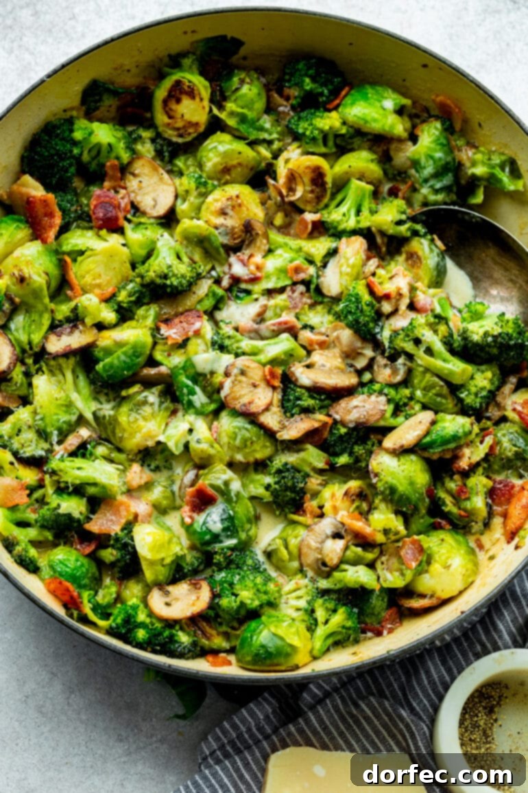 a photo of a large skillet full of cooked brussel sprouts, broccoli, mushrooms, and crispy bacon all mixed with a creamy sauce.
