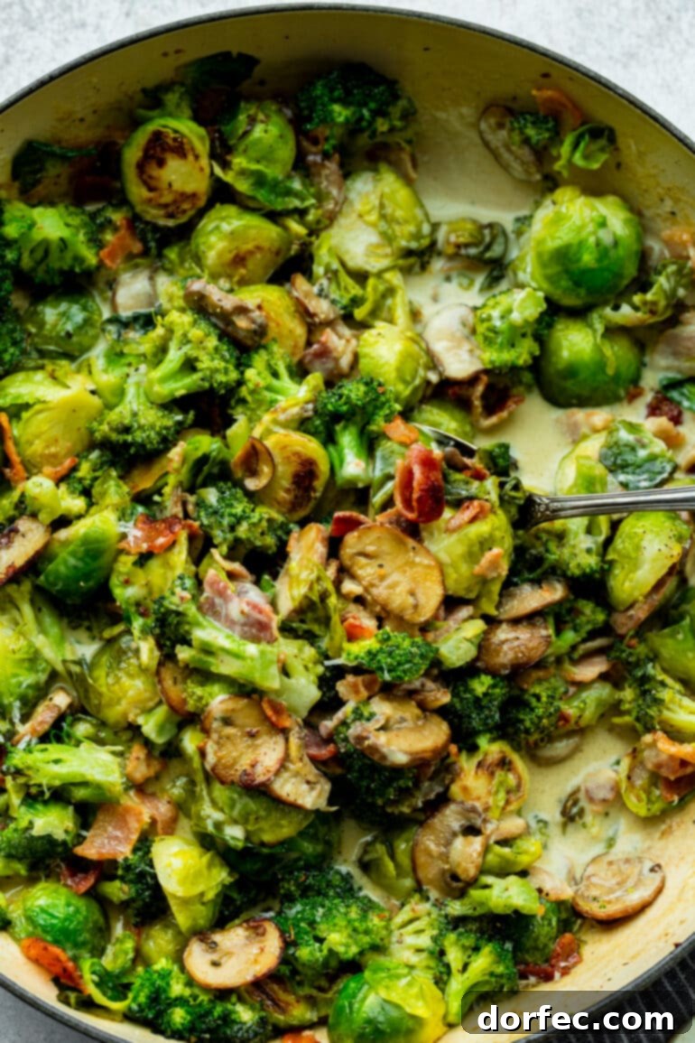 a photo of halved brussel sprouts, sliced mushrooms, broccoli florets and crispy bacon bits being sauteed in a cast iron skillet with a creamy sauce